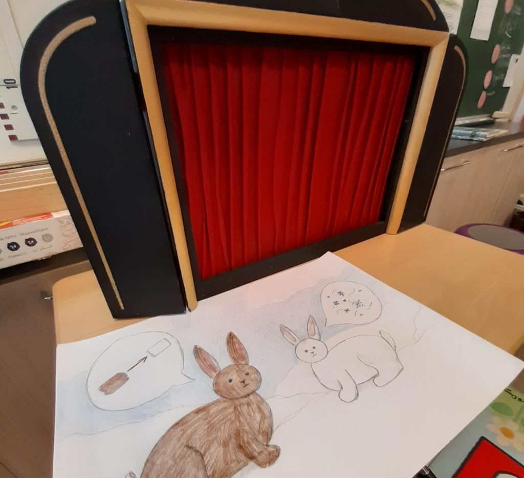 Edessä paperille piirretyt jänikset, takana punaiset nukketeatterin verhot